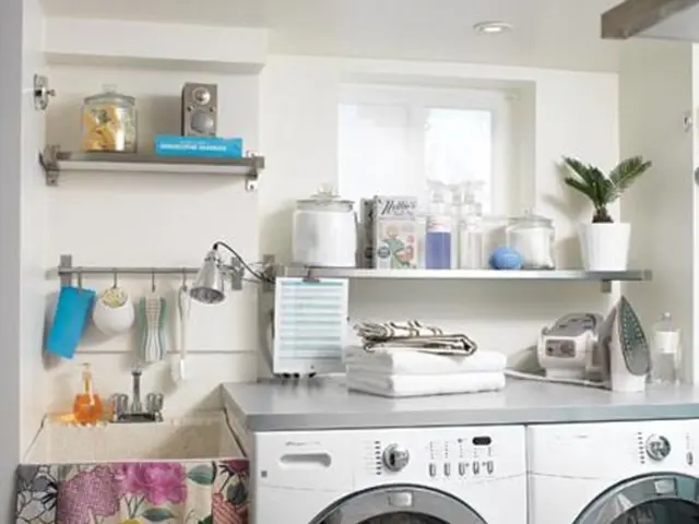 In this image, in the middle there are two washing machines, iron box, clothes, shelves, vessels,...