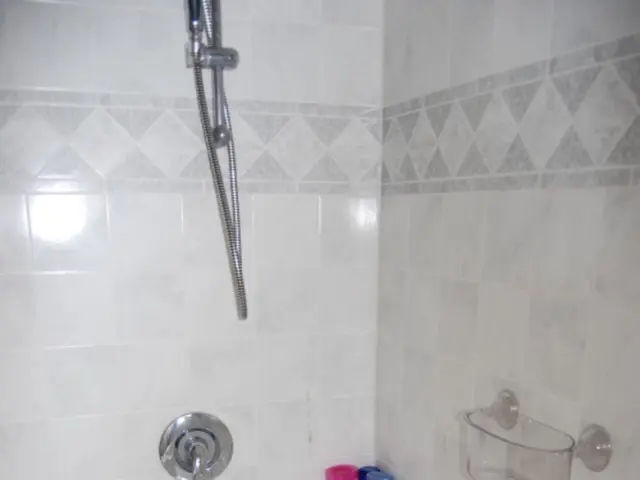 There is a bathtub. There are bottles, soap stand and a hand shower. There are white tiles.