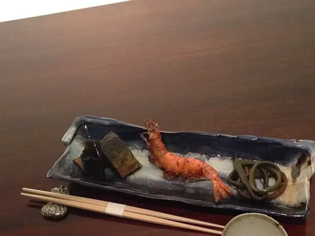 In this image we can see chopsticks and prawns in bowl placed on the table.